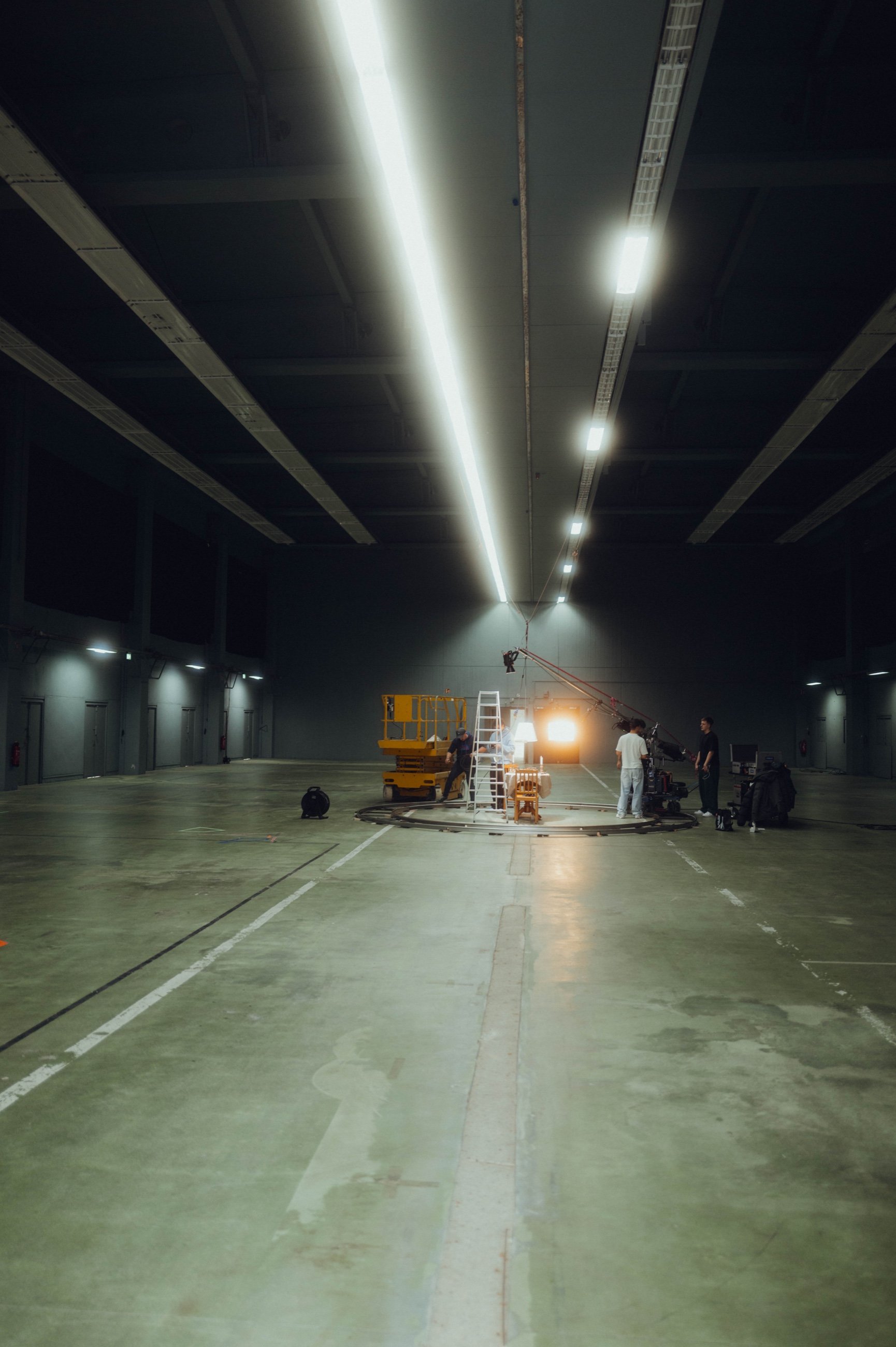 Leere Halle mit Lichtband an der Decke, am Ende baut eine kleine Crew einen Dolly-Kreis auf