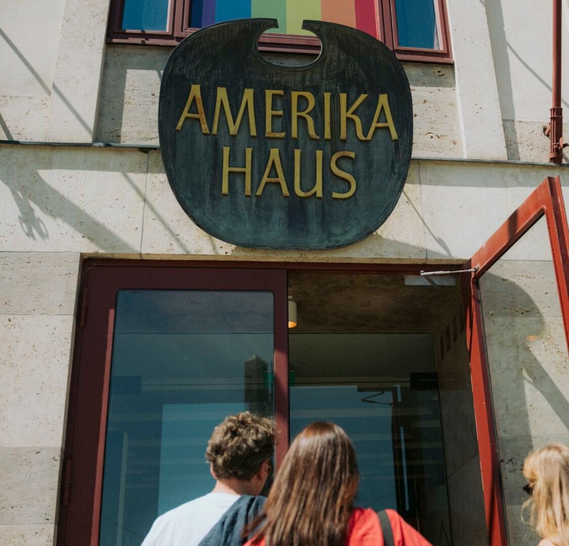 Eingang des Amerikahauses München mit dem bronzenen Schild über der Tür, davor Gäste beim Hineingehen