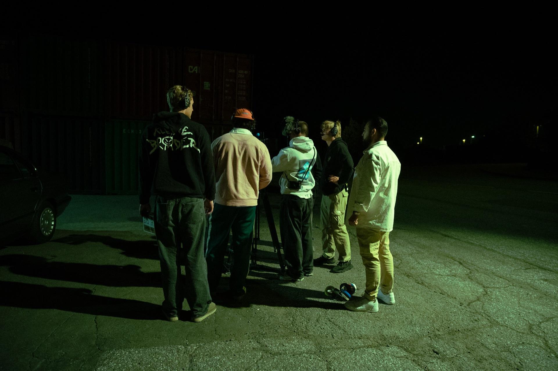 Behind the scenes: the team gathers at night in front of the wall of containers, a film light illuminating the lot