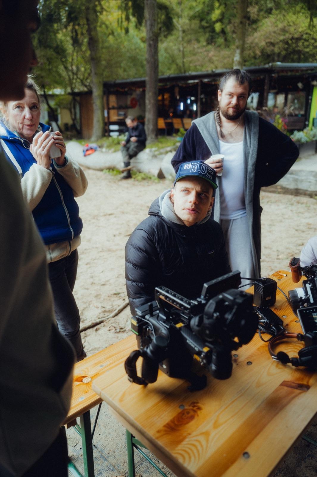 Behind the Scenes: der Kameramann mit Cap an der Kamera auf einem Biertisch, Crew-Mitglieder drumherum