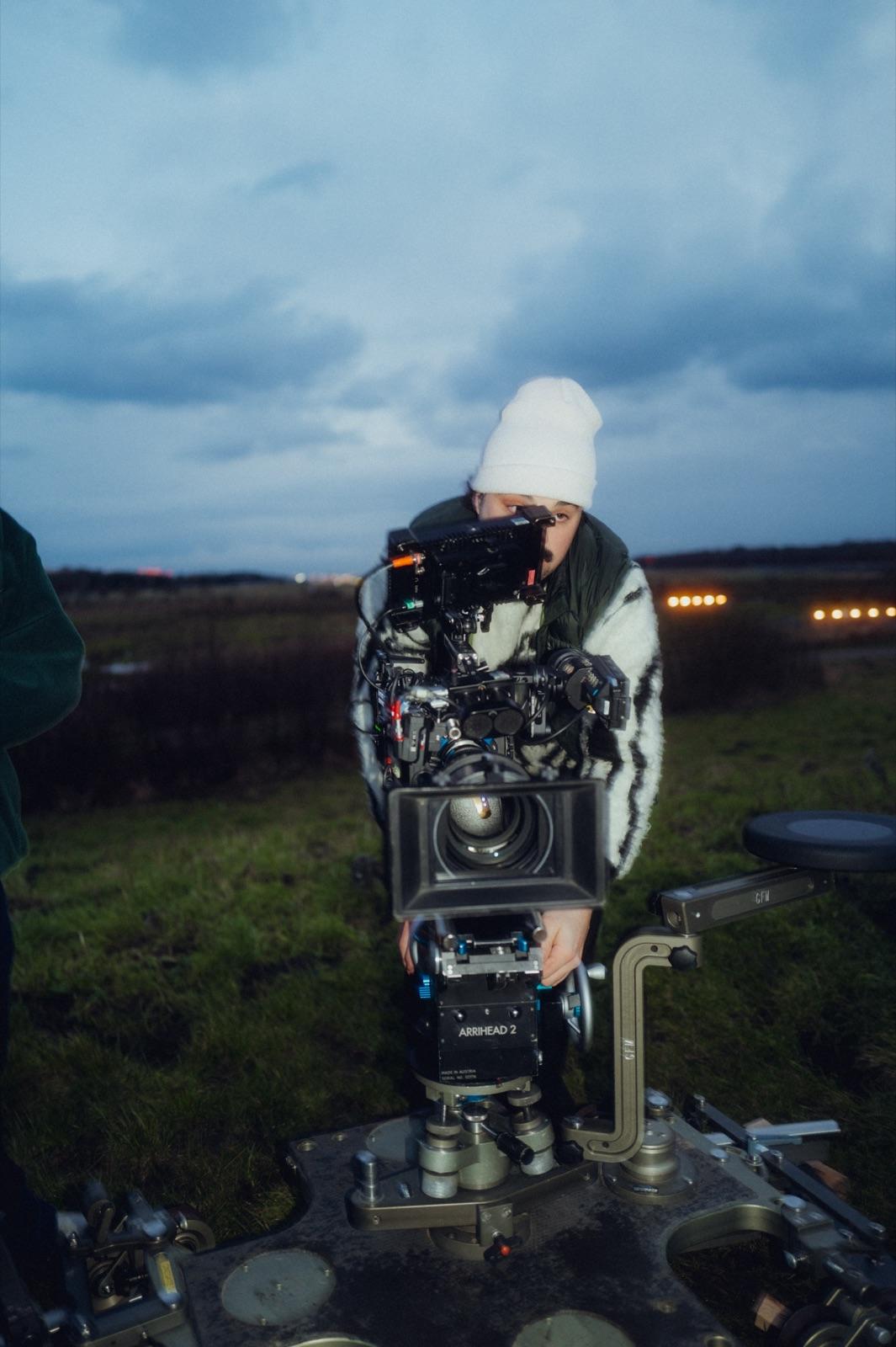 Behind the Scenes: ein Operator mit weißer Mütze blickt durch die ARRI auf dem Dolly, dahinter die Lichterkette