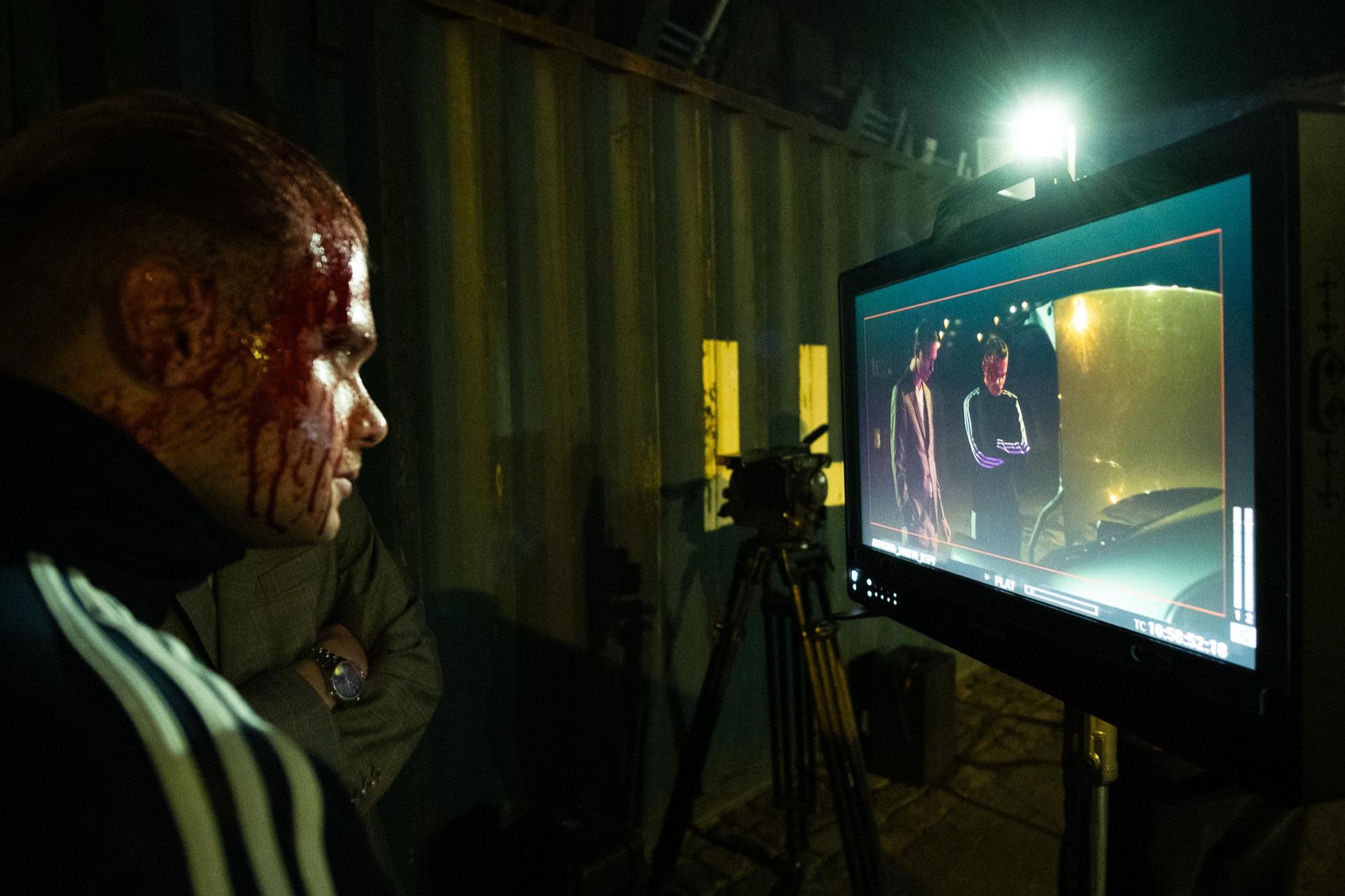 Behind the scenes: the actor with blood make-up looks in profile at the monitor next to the camera