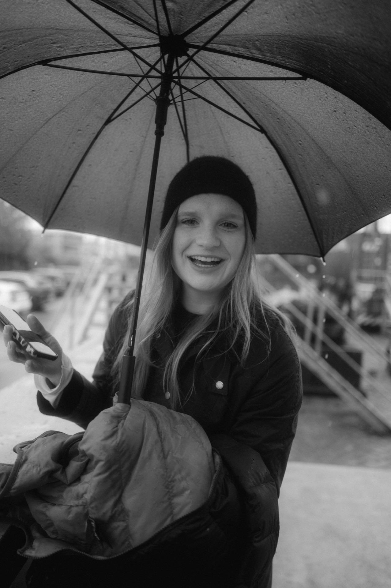 Behind the Scenes: ein Crew-Mitglied lächelt unter einem aufgespannten Regenschirm im Hafen
