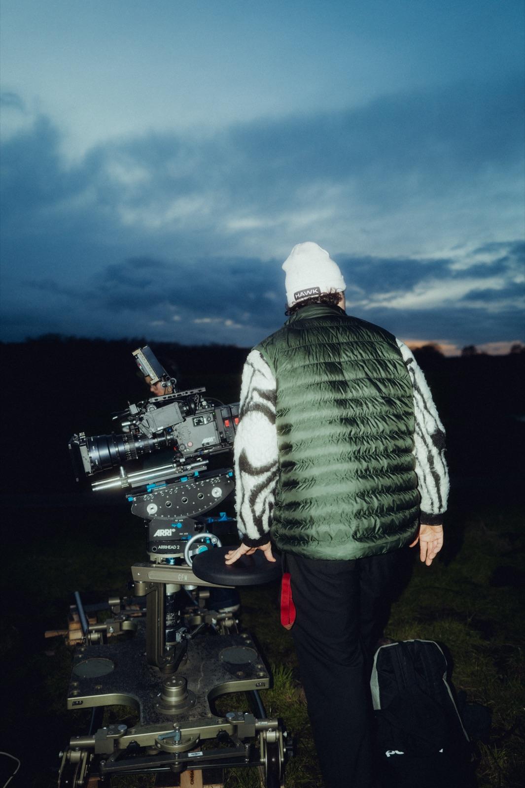 Behind the Scenes: ein Operator in Felljacke schiebt den Dolly von hinten zur blauen Stunde