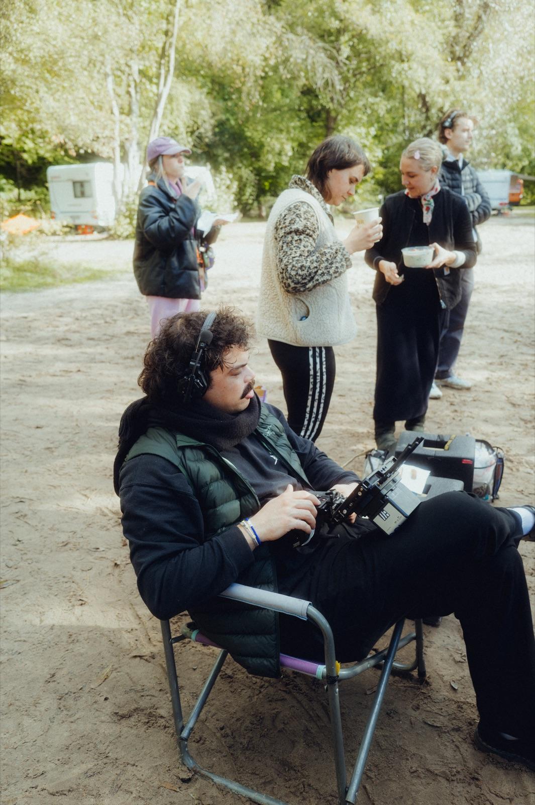 Behind the Scenes: der Tonmann mit Kopfhörern sitzt am Recorder, dahinter Crew mit Kaffeebechern am Campingplatz