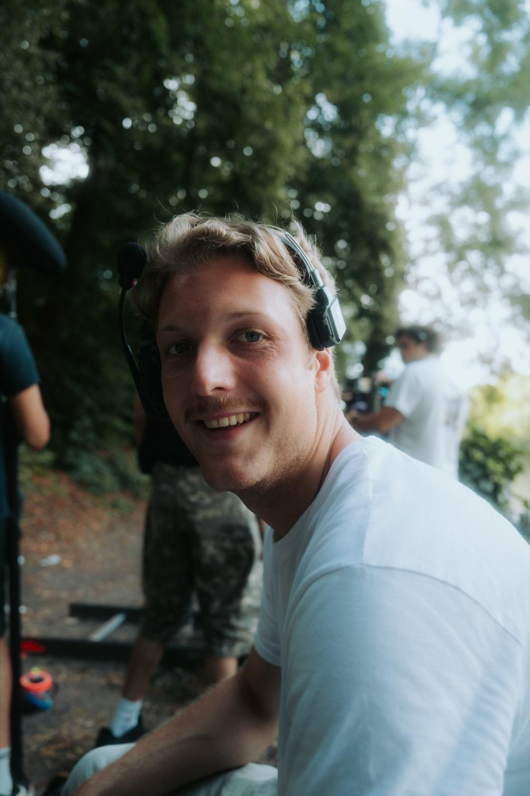 Behind the Scenes: ein Crew-Mitglied mit Kopfhörern lächelt warm in die Kamera, hinter ihm die Geräte-Cases im Hof