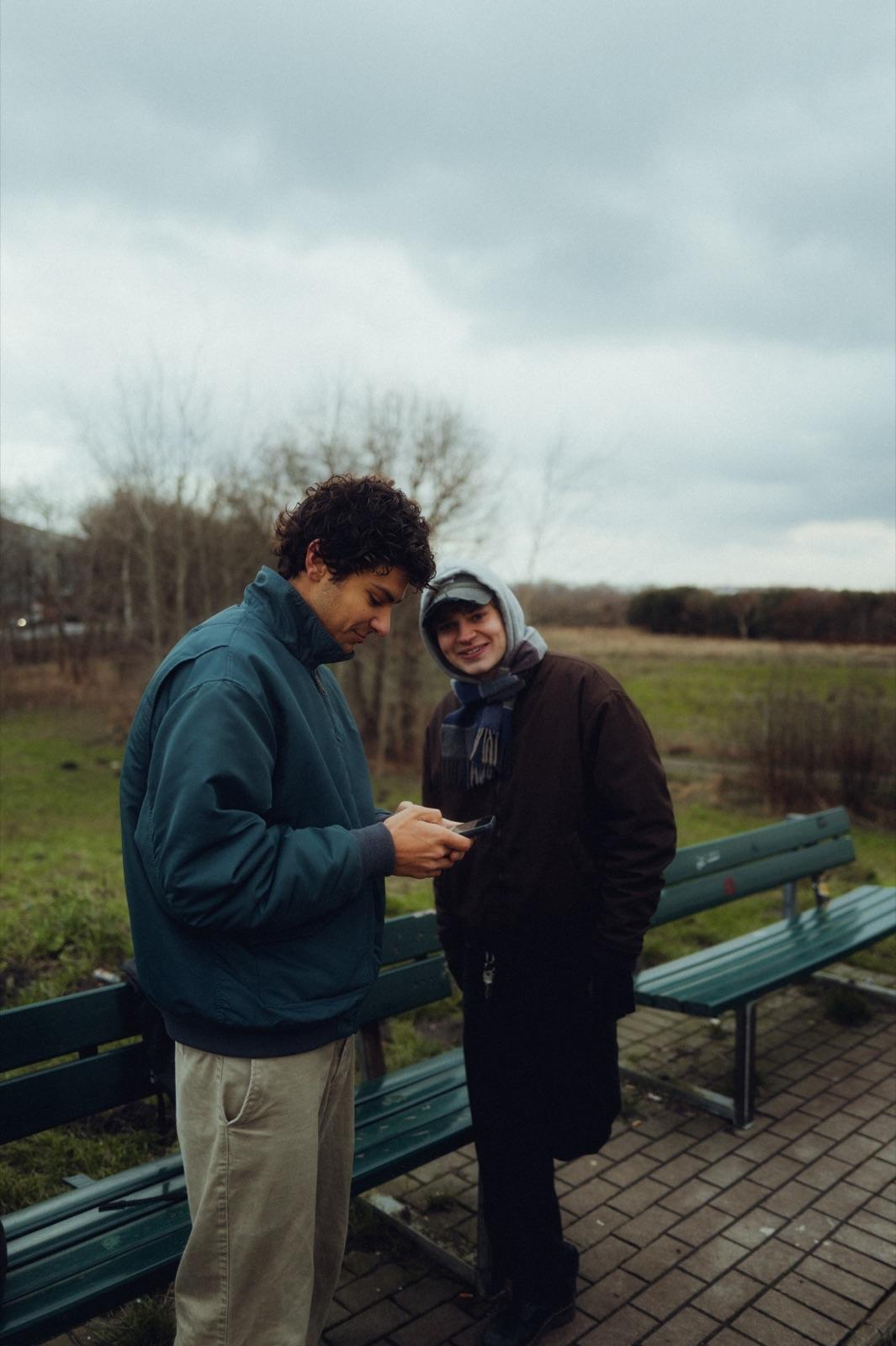 Behind the Scenes: zwei Crew-Mitglieder an einer Bank, einer zeigt dem anderen lächelnd etwas am Gerät