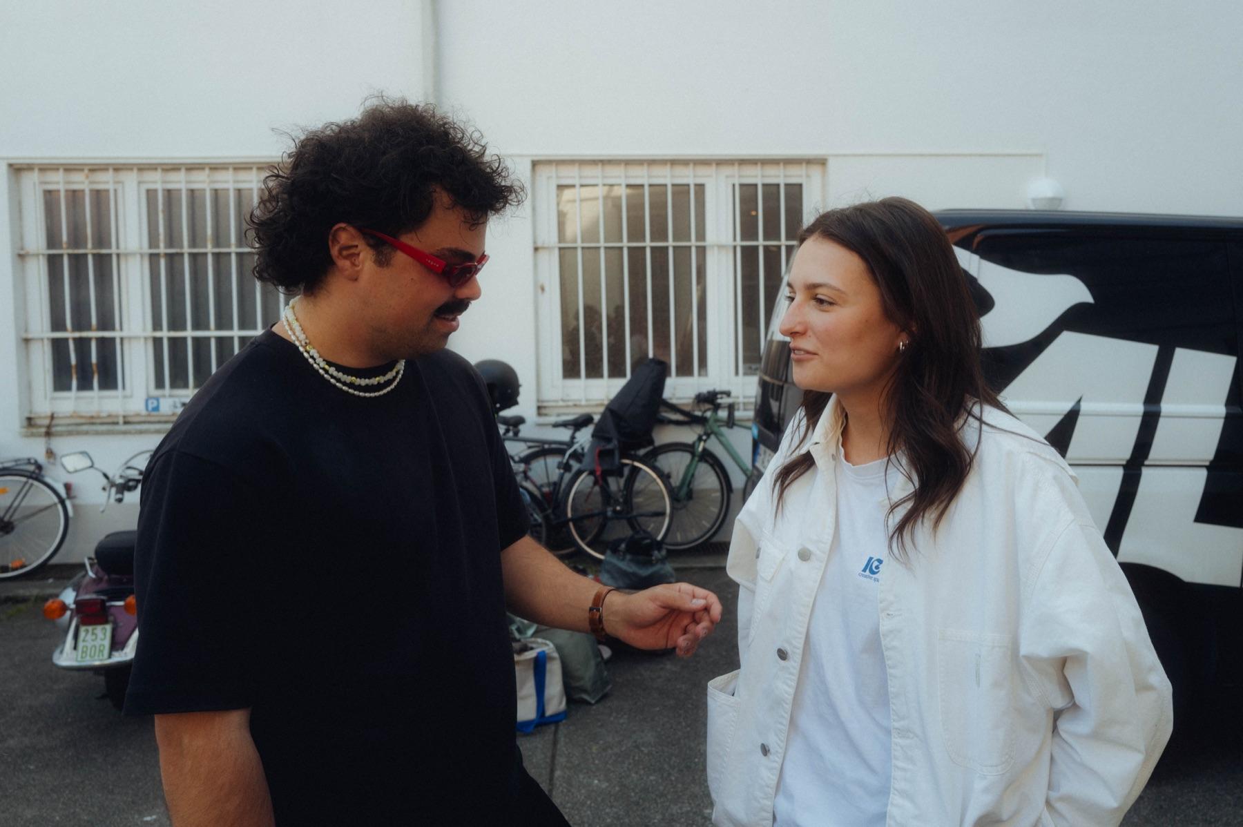 Behind the scenes: two crew members in conversation in warm evening light, a man with red glasses and a woman in a light jacket