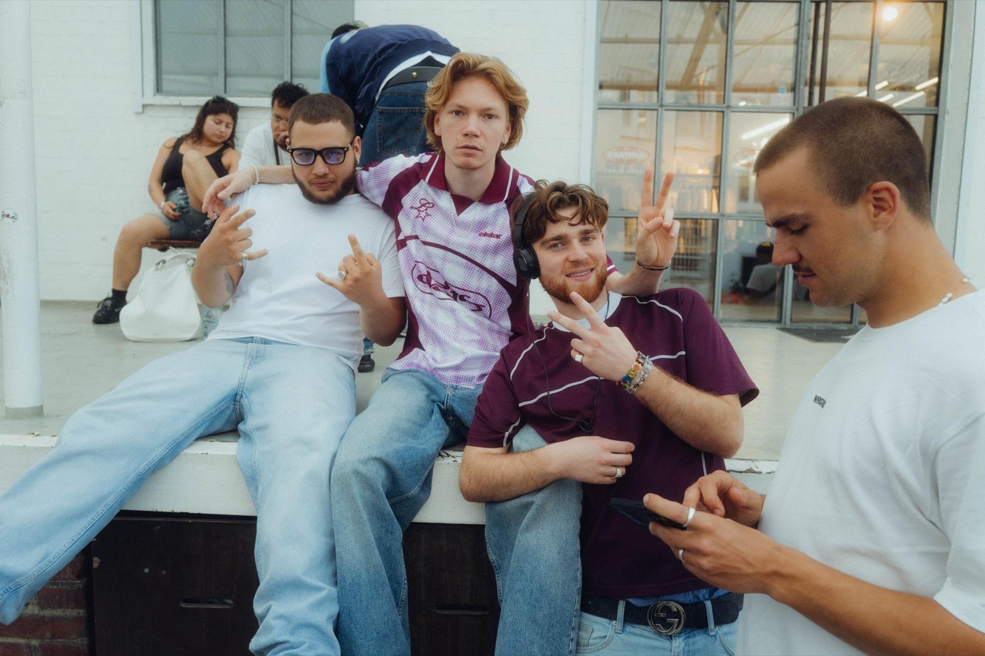 Behind the scenes: four young men sit relaxed on a wall flashing peace signs, one in the burgundy Elstar jersey