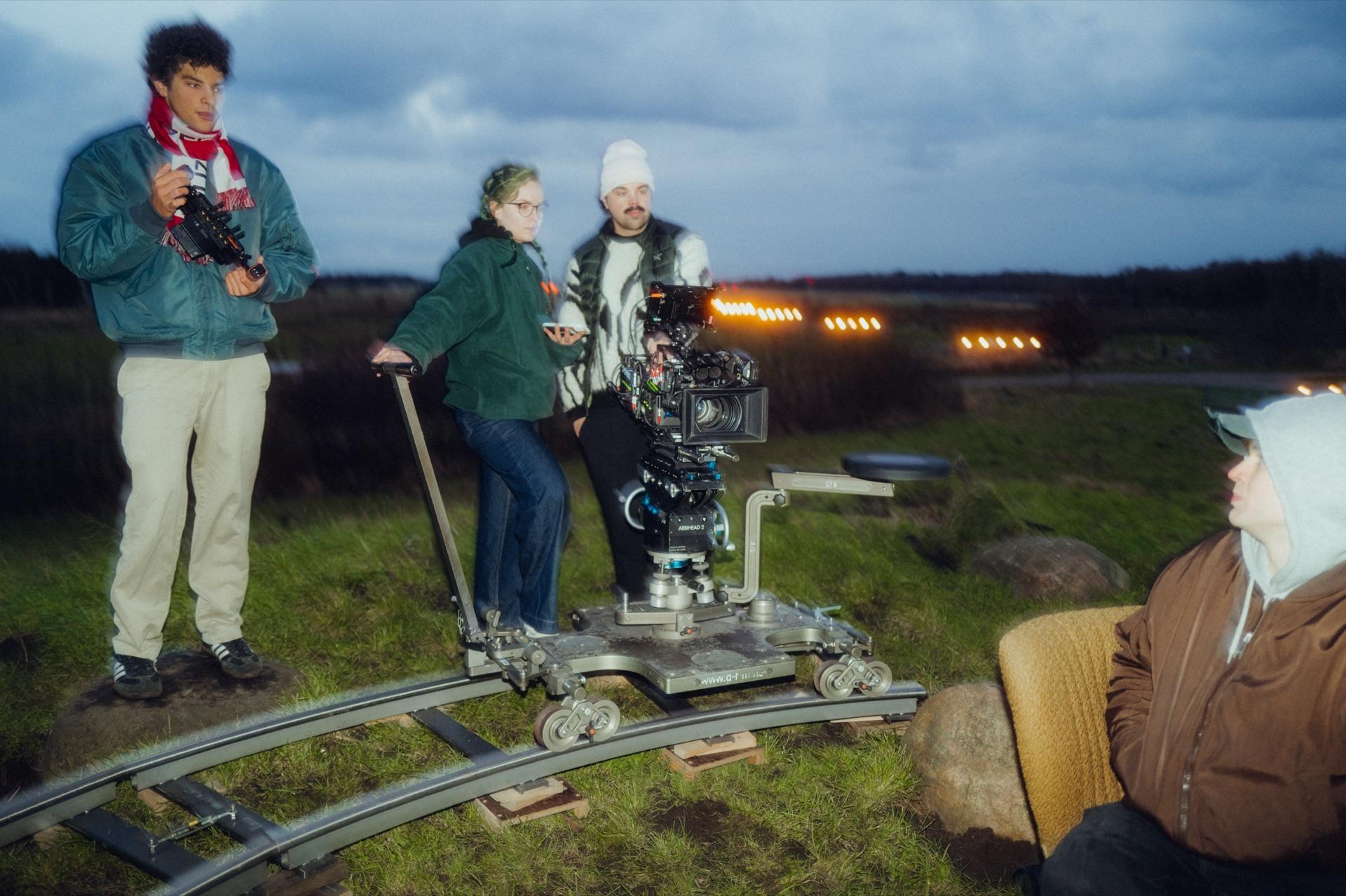 Behind the Scenes: das vierköpfige Team rund um den Dolly auf der halbkreisförmigen Schiene zur blauen Stunde, im Hintergrund eine Reihe Lichter