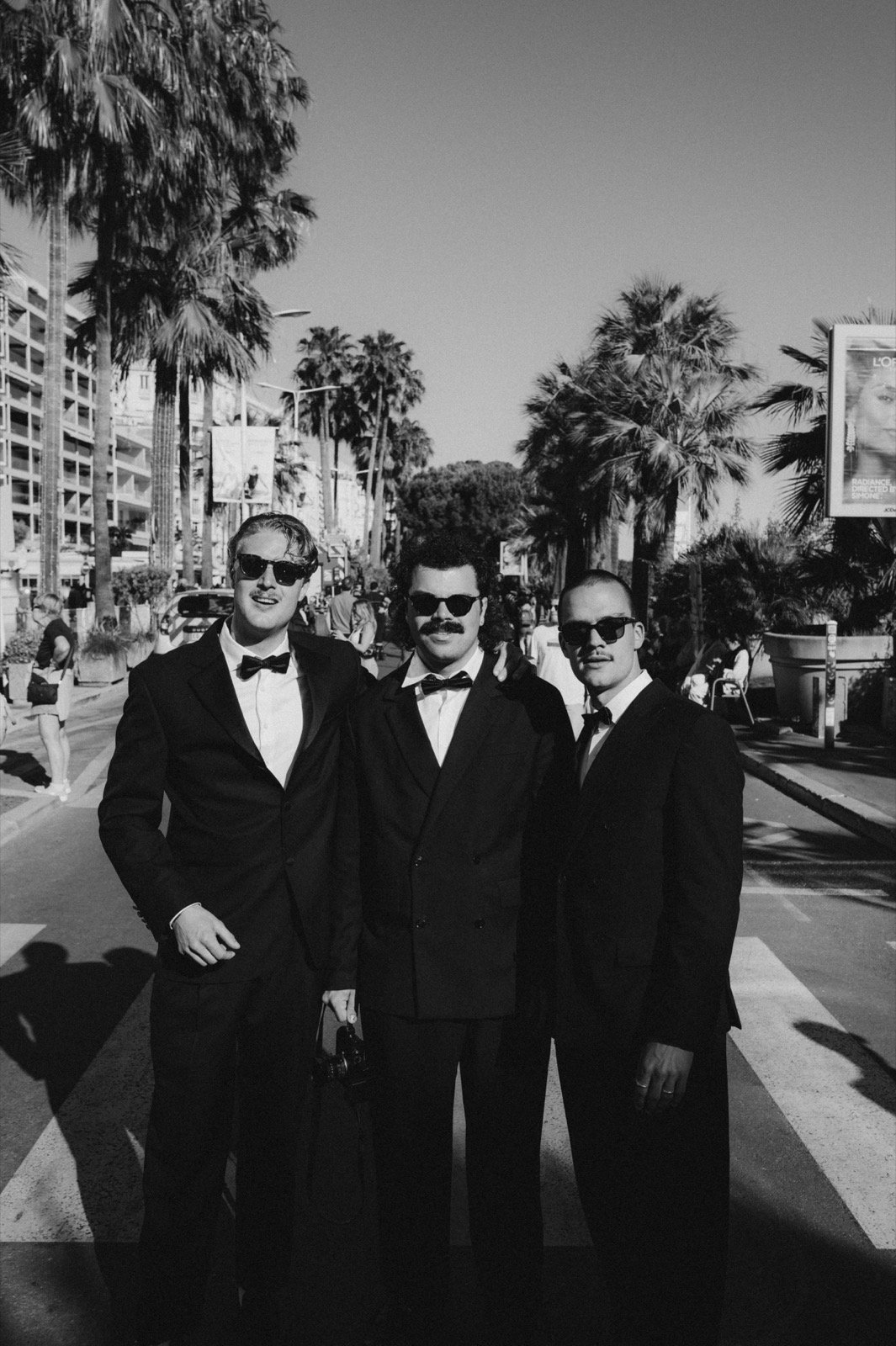 Jakob Hermann Haehner, Lino Kalkhoff und Johannes Fielers im Smoking vor Palmen an der Croisette, schwarzweiß
