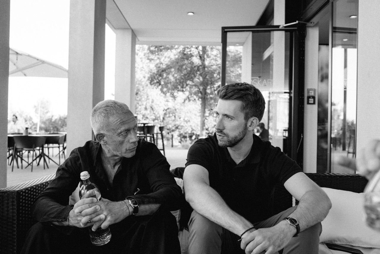 Two men sitting in conversation on a covered terrace