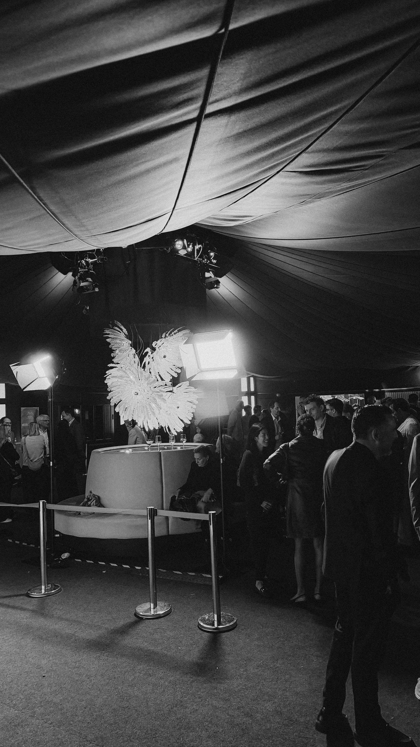 Inside the tent with spotlights under the ceiling, a round banquette and a light object made of feathers