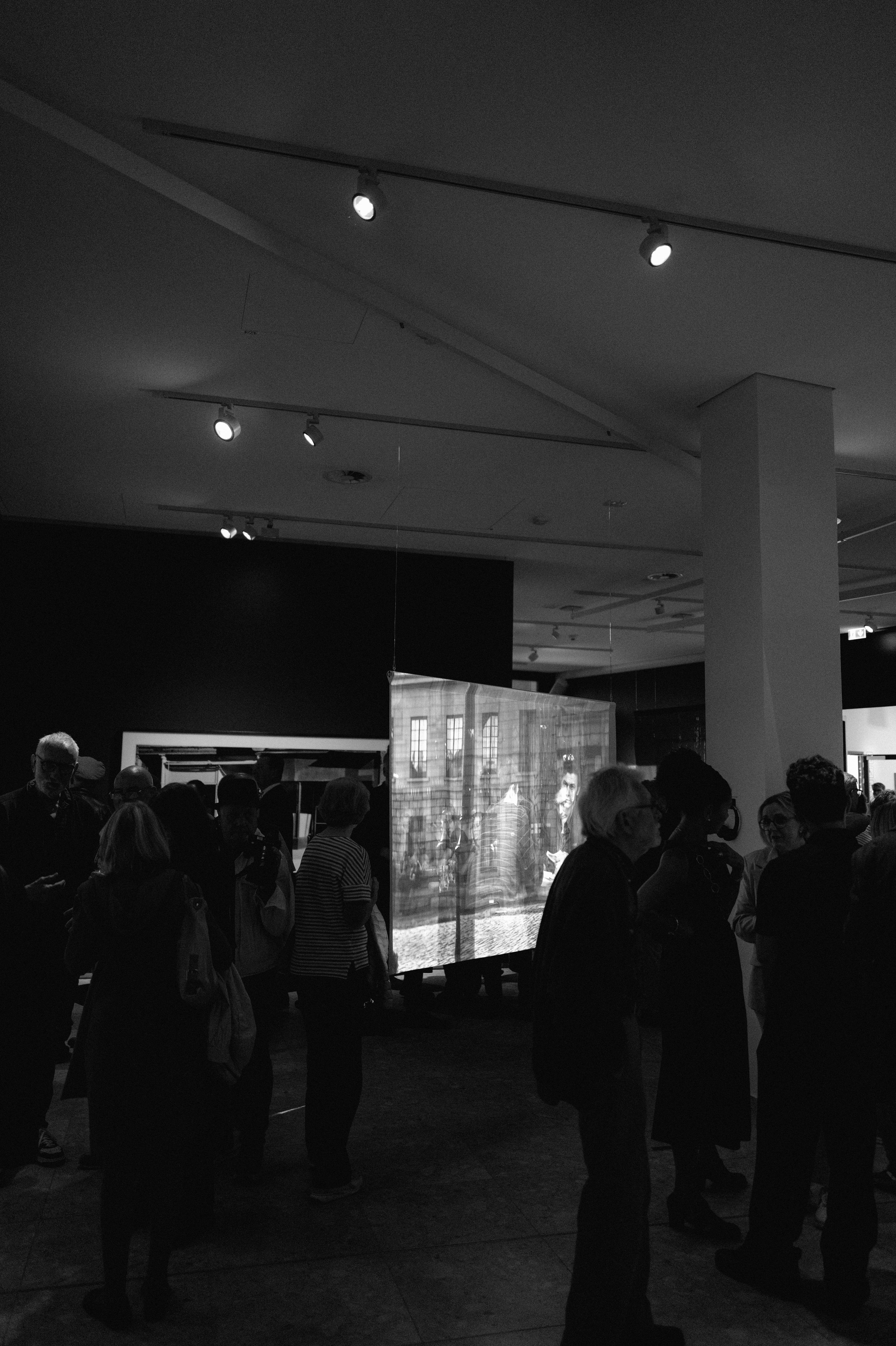 Besucher vor einer auf transparenten Stoff projizierten Fotografie, die frei im Raum hängt