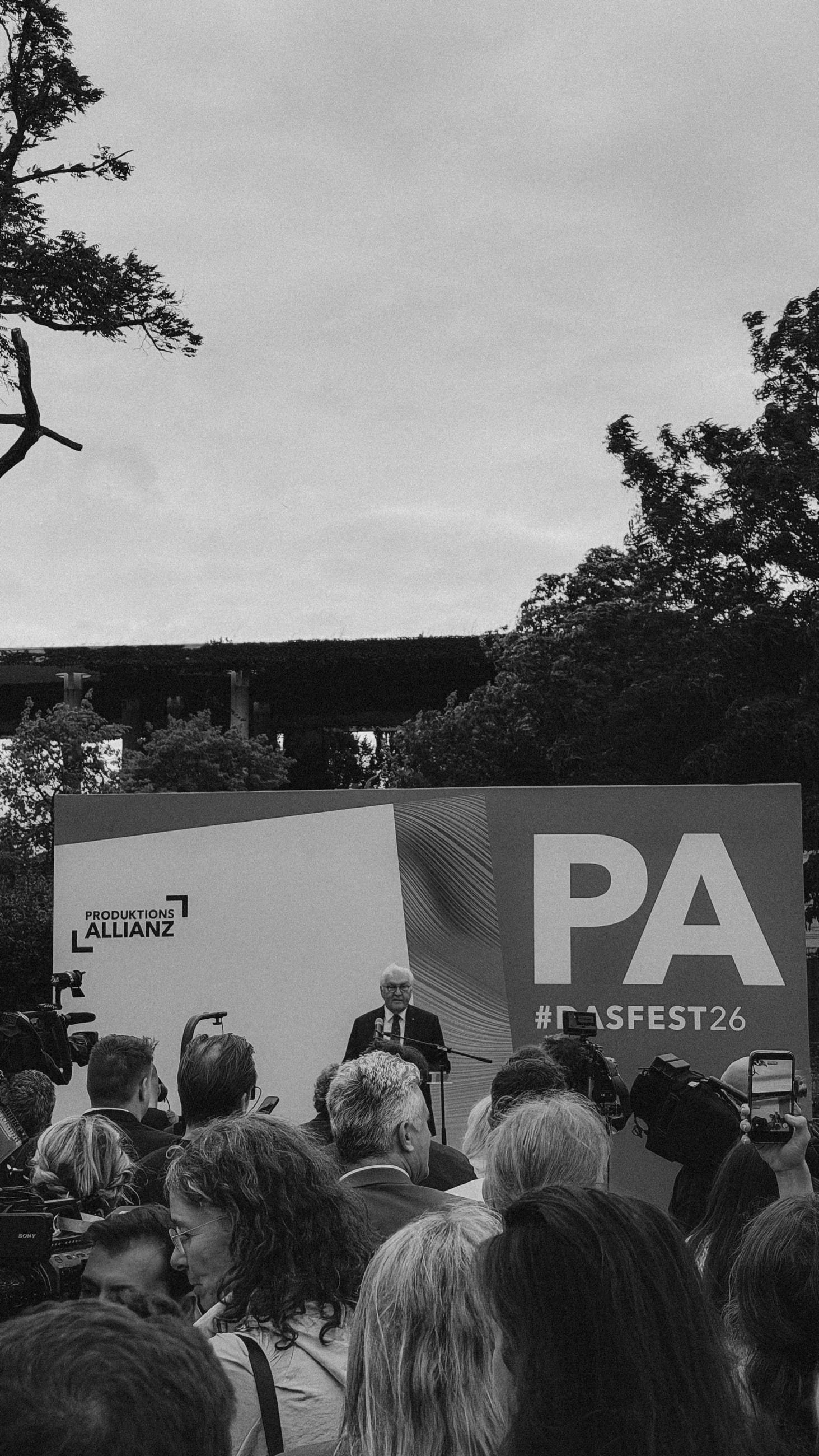 A speech at the lectern in front of the stage wall with the Produktionsallianz logo and the hashtag „#DASFEST26“, an audience and television cameras in front of it