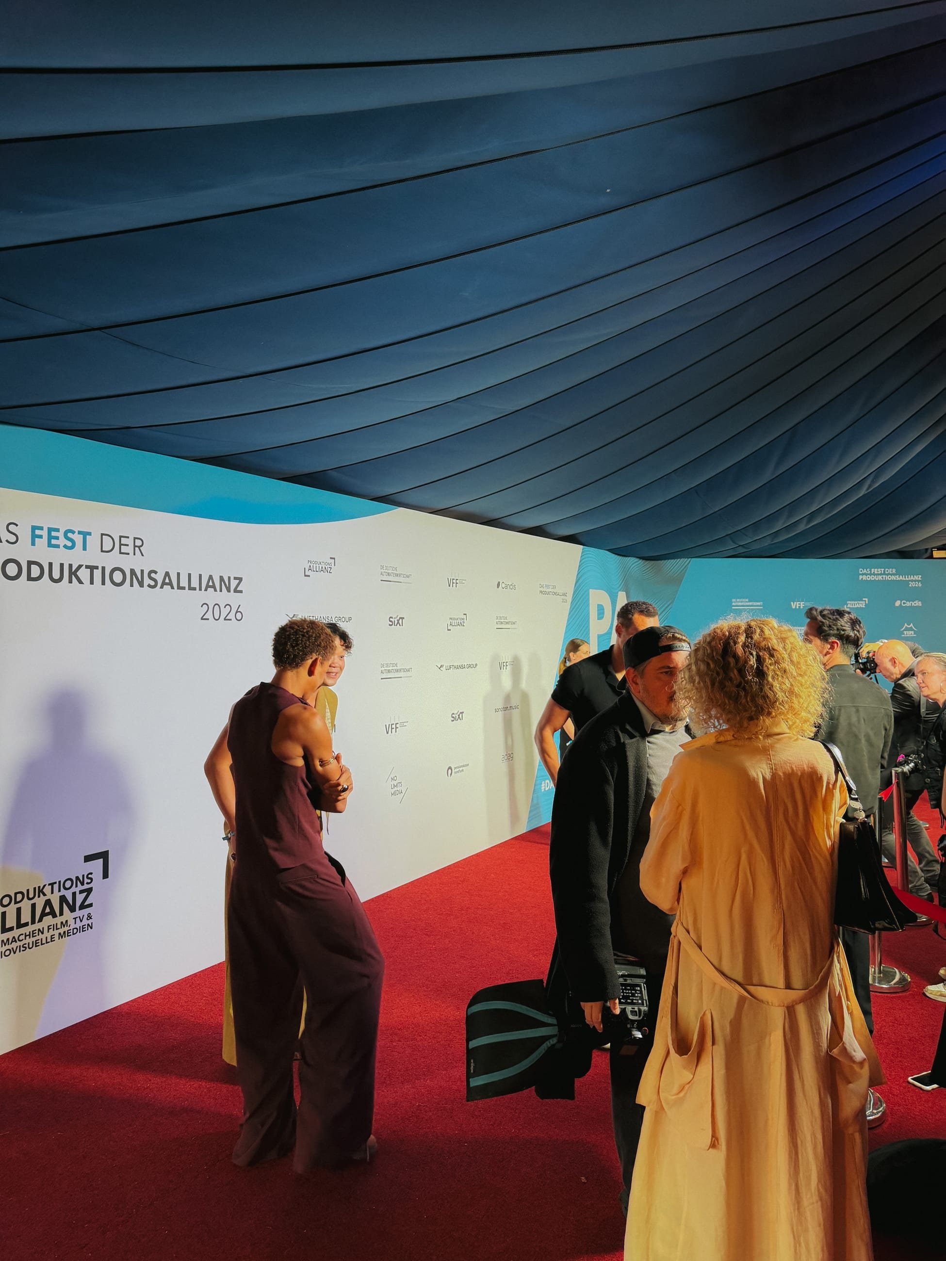 Red carpet in front of the partner wall inside the tent, guests talking, a photographer with a camera on the right