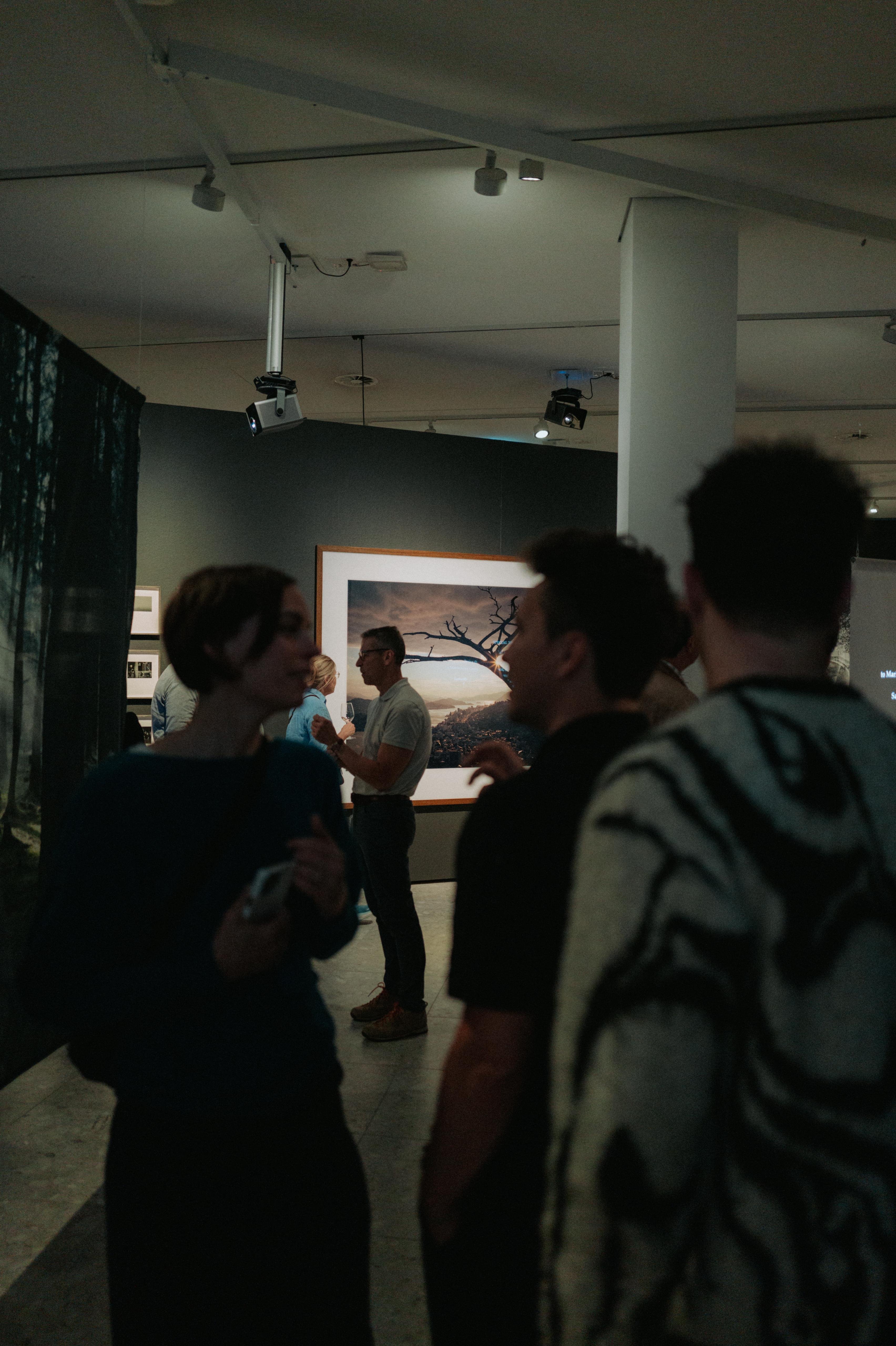 Besucherinnen und Besucher der Vernissage vor einer großformatigen, farbintensiven Landschaftsfotografie von Wim Wenders