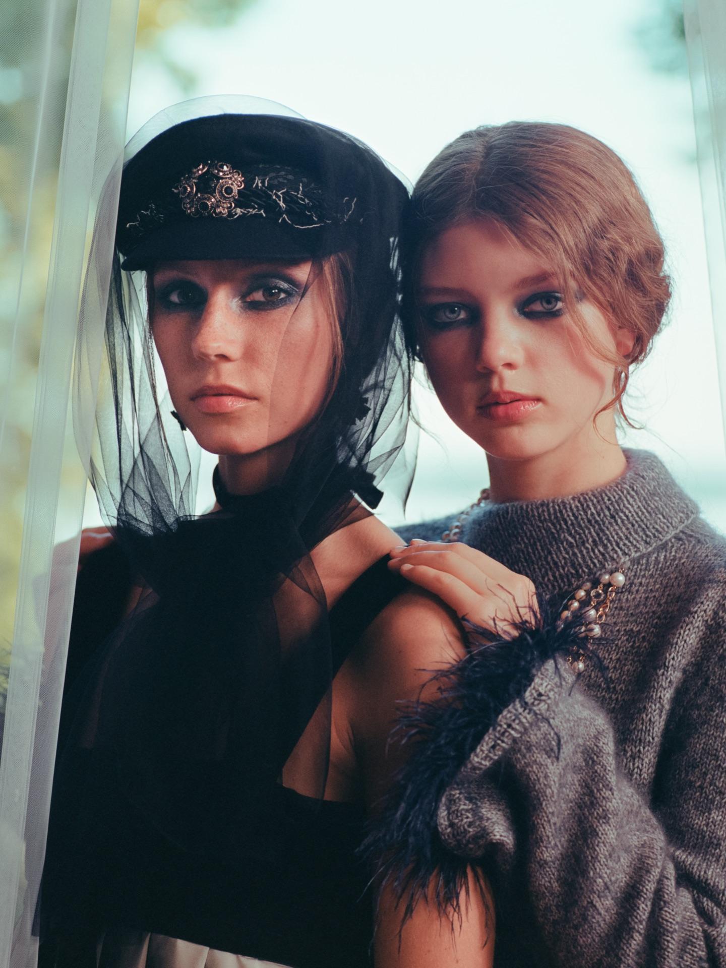 Two models in dark gowns with hats and veils, close together