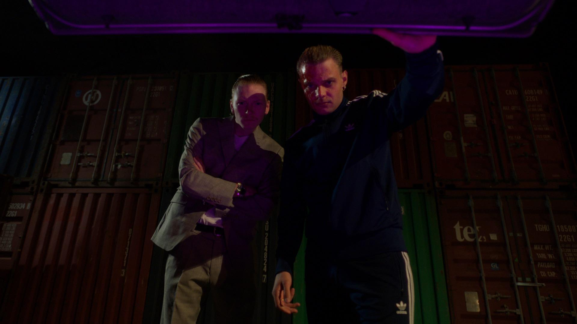 Two figures at an open car boot, lit from below in the purple glow of the lid