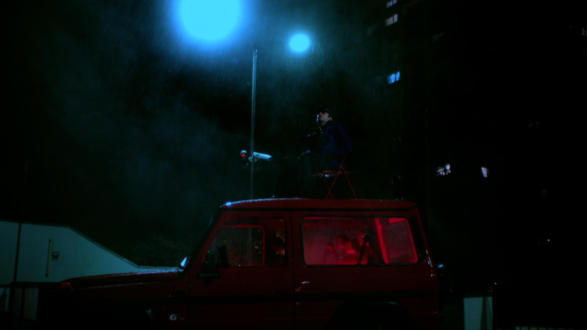 Jaschu sits on the roof of the red pickup under blue streetlight