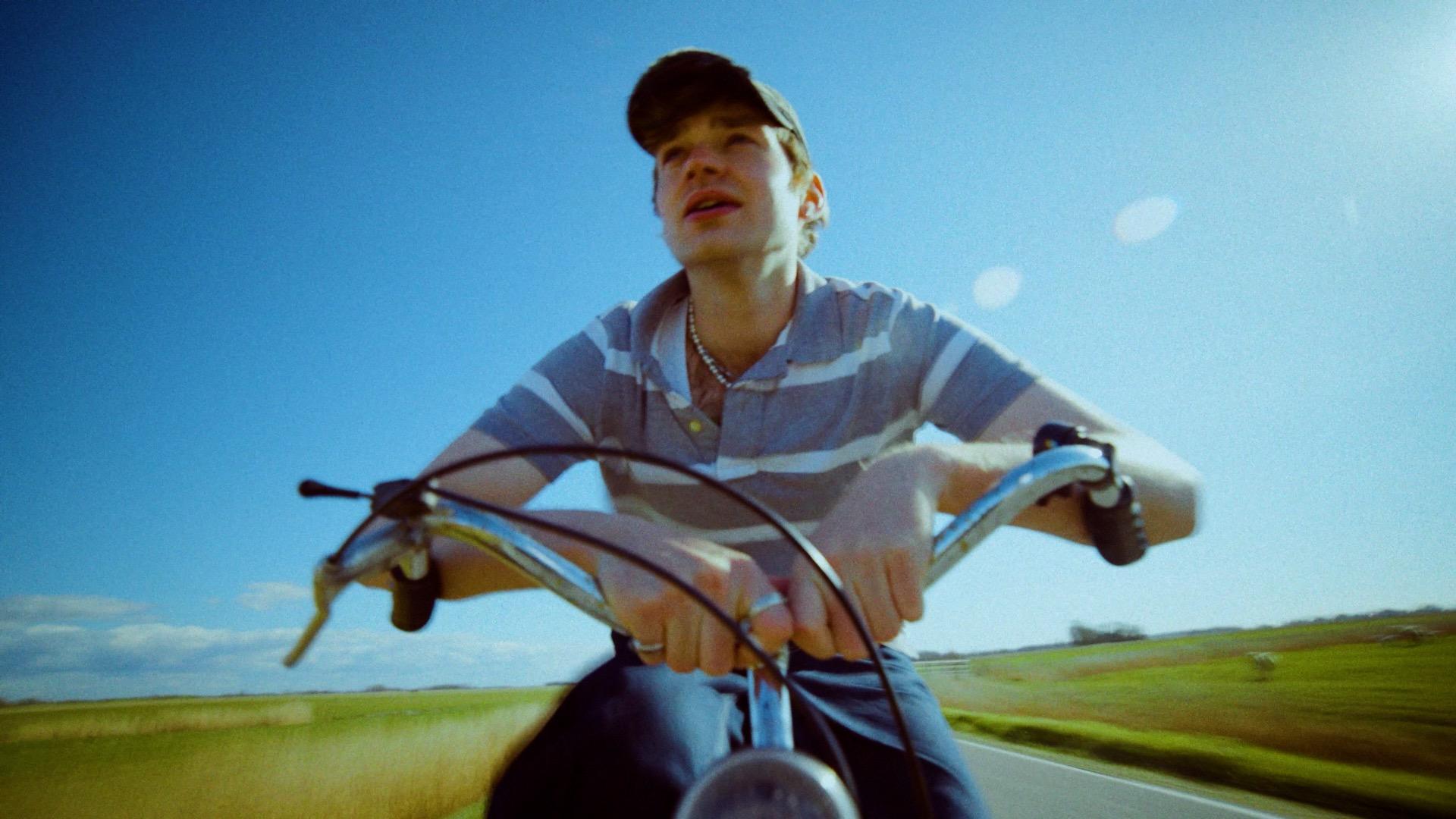 Radfahrer von vorn vor weitem Feld und blauem Himmel