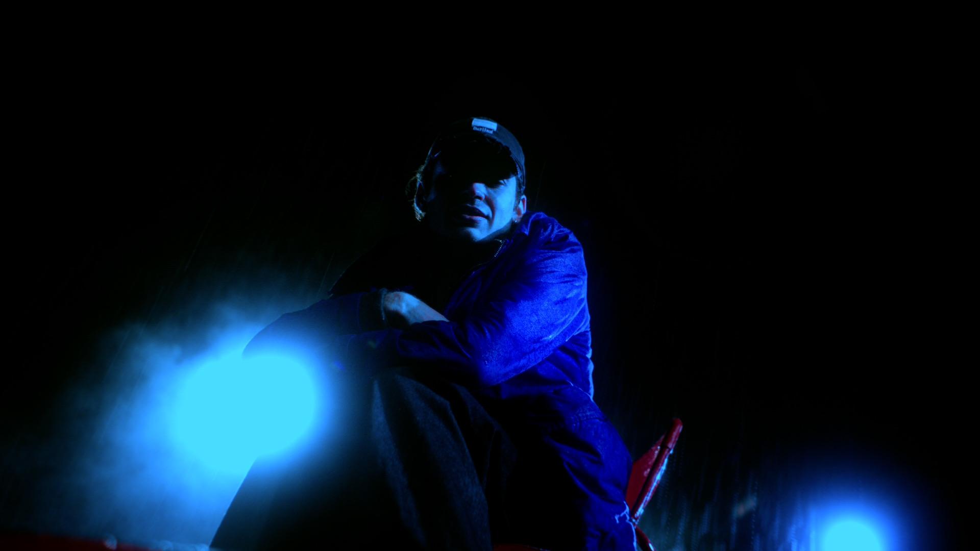 Close shot of Jaschu, bathed in blue backlight, crouching