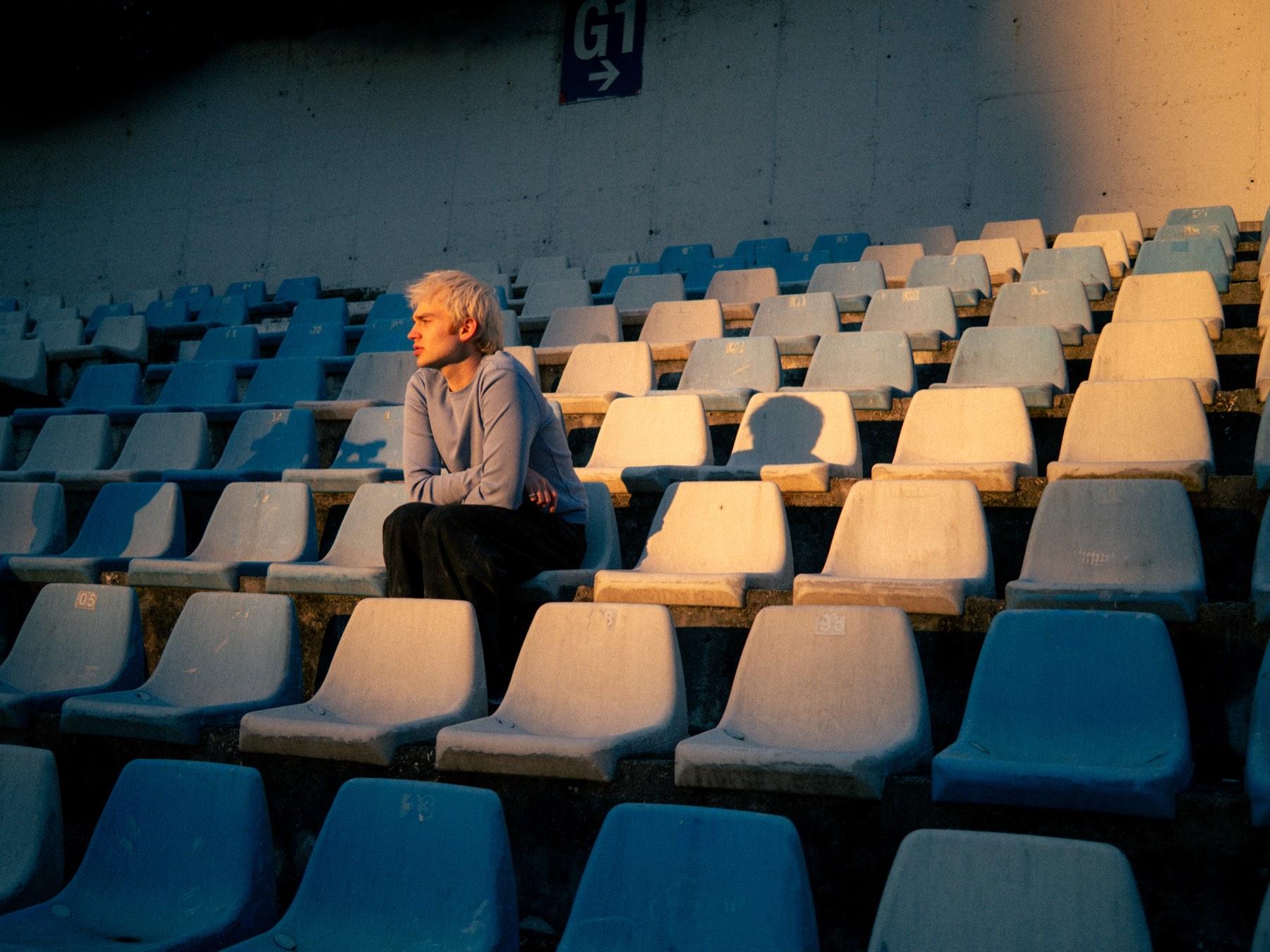 Jaschu sitzt allein in leeren Stadionrängen im warmen Abendlicht