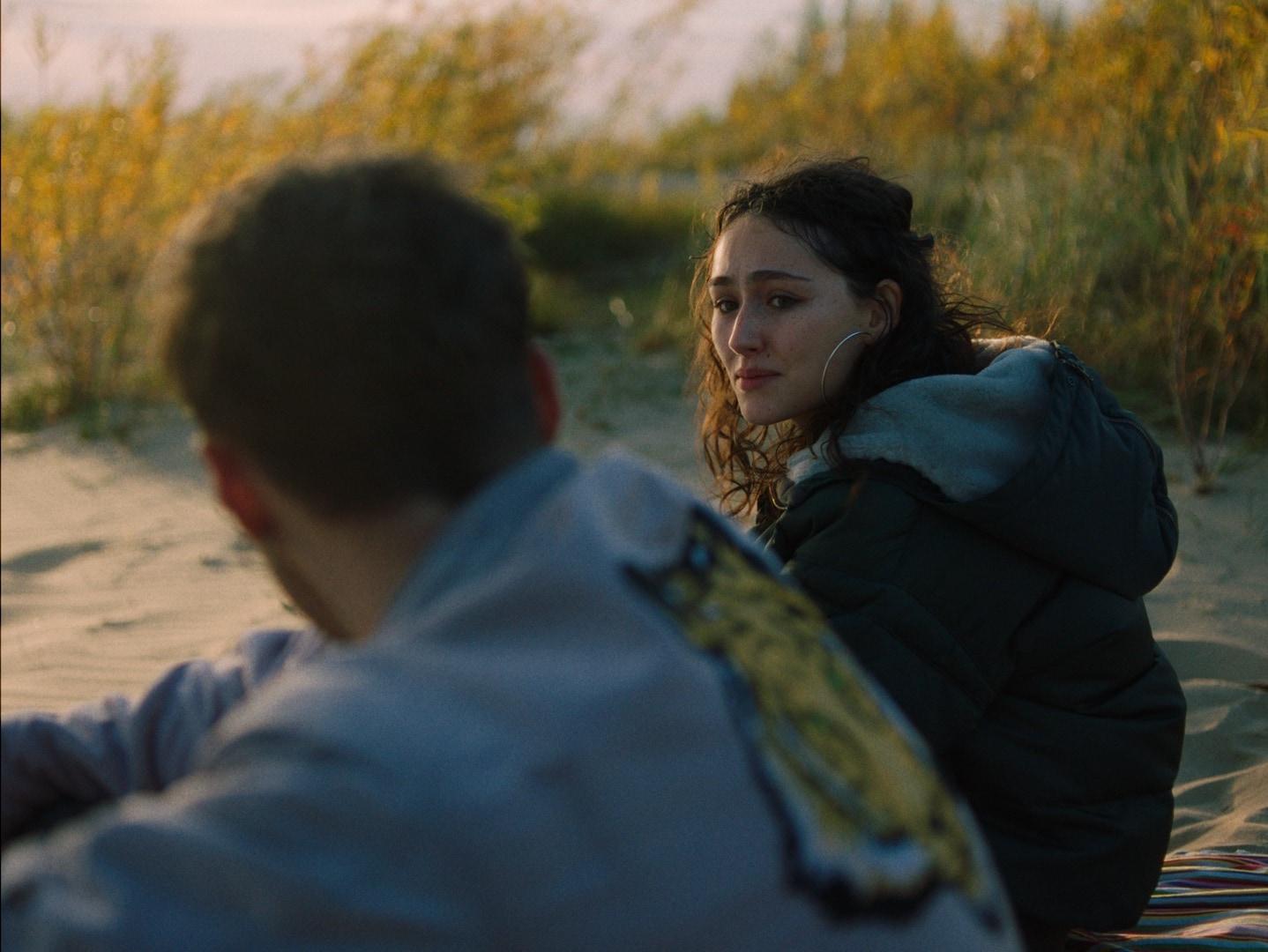 Mina und Leo sitzen am Strand in den Dünen und sehen sich an