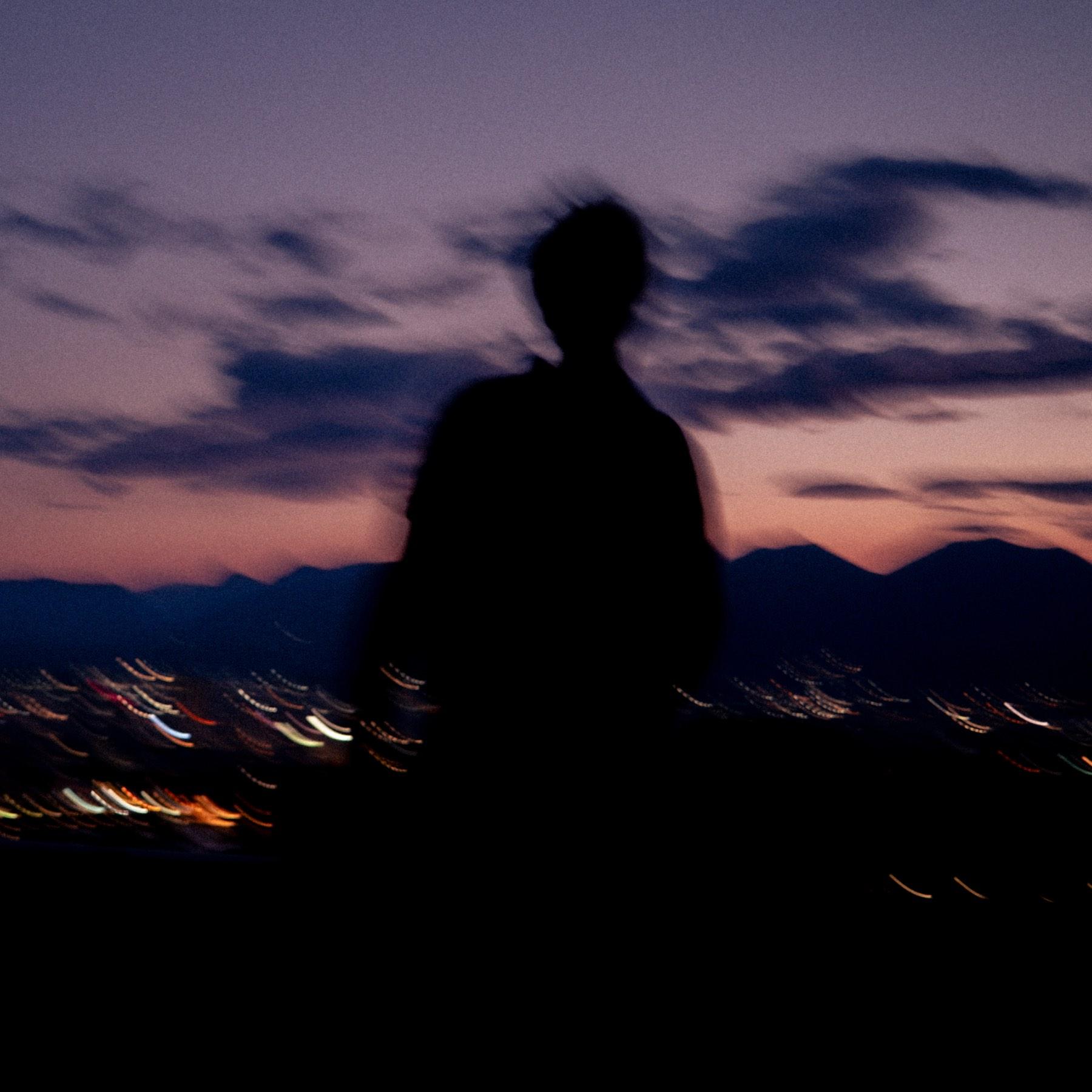 Jaschu als verwischte Silhouette vor dem letzten Licht des Tages und fernen Stadtlichtern