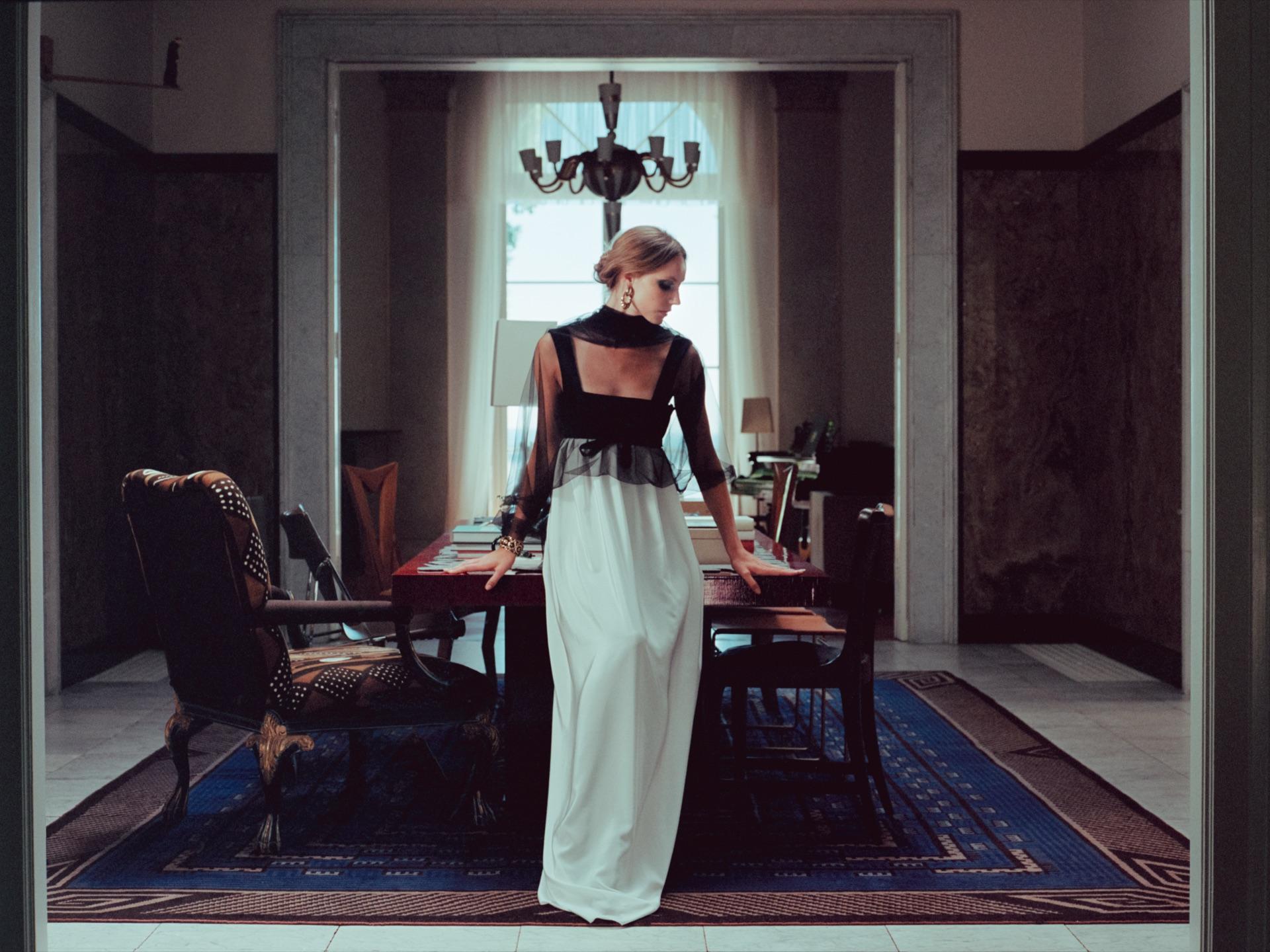 Model in a light-coloured gown in a dining hall beneath a chandelier