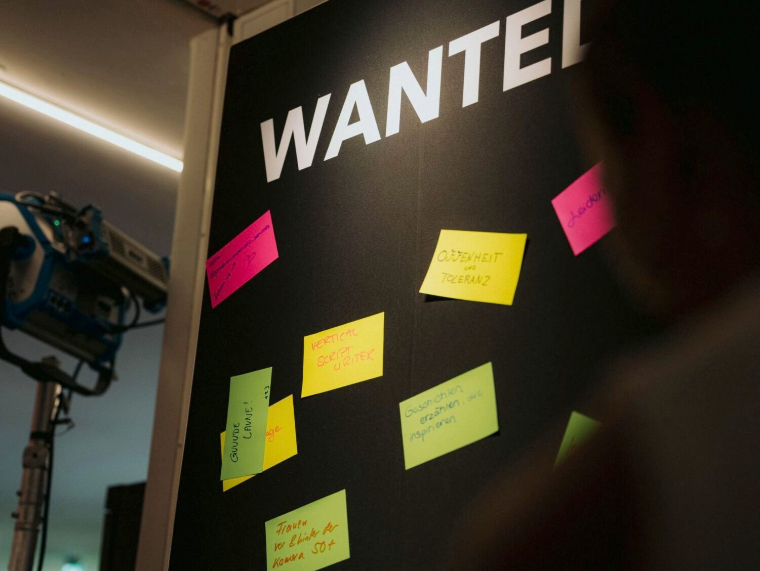 Schwarze Stellwand mit dem Schriftzug Wanted, darauf bunte Post-its mit handschriftlichen Notizen der Gäste