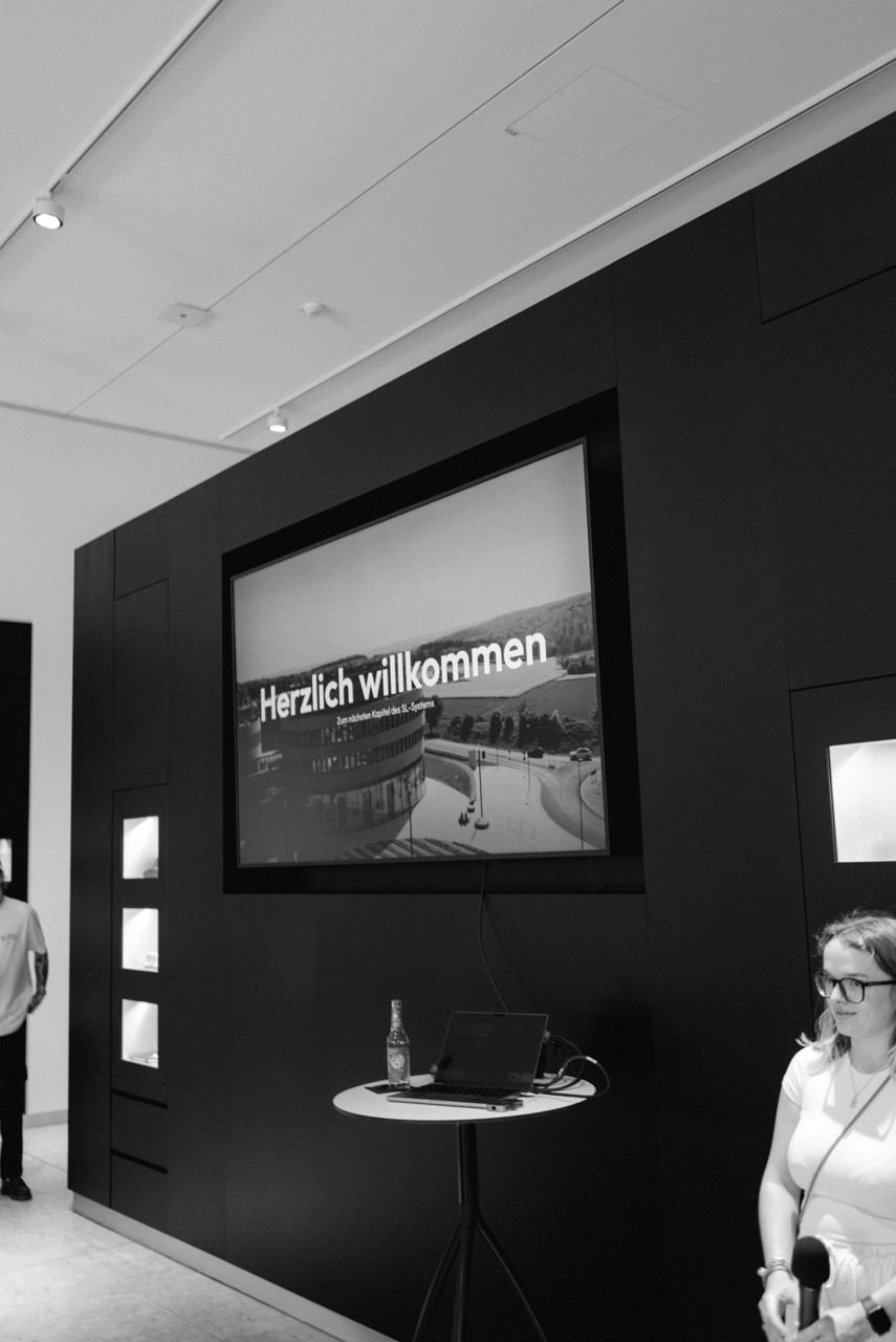 Screen reading „Herzlich willkommen. Zum nächsten Kapitel des SL-Systems“ in a darkened exhibition room